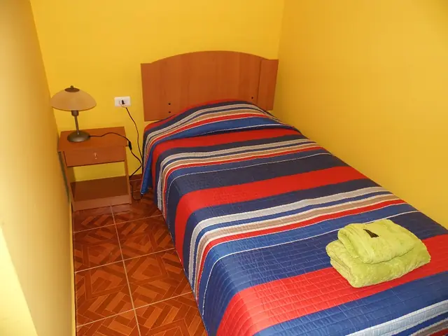 Cama single con cubrecama a rayas y velador